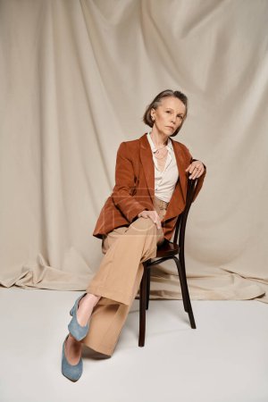 Mature woman in tan jacket and pants sitting comfortably on chair.