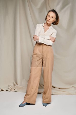 Photo for A mature woman in a stylish white blouse and tan trousers poses gracefully. - Royalty Free Image