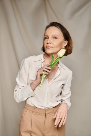 A stylish woman in white shirt and tan pants holding a tulip.