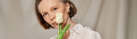Téléchargez les photos : Une femme mature en tenue décontractée tenant une fleur dans sa bouche tout en posant énergiquement. - en image libre de droit