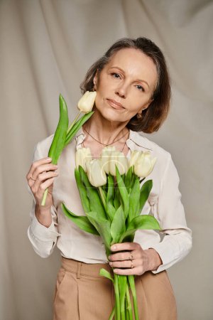 Reife Frau hält freudig einen Strauß weißer Tulpen in der Hand.