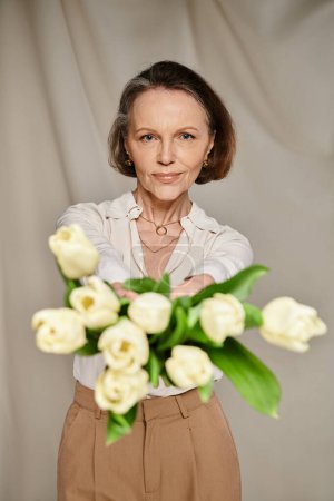A mature woman gracefully holds a bouquet of white tulips, exuding elegance and grace.