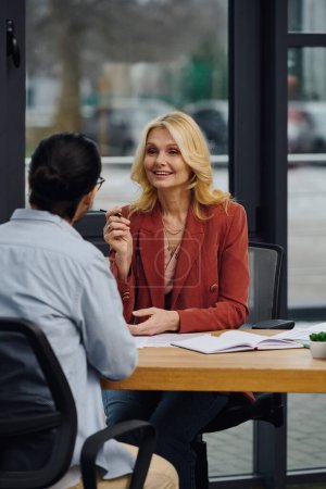 Woman and man conversing at table in office setting.