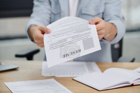 A job seeker holds up a paper at a desk.