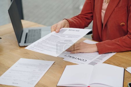 Téléchargez les photos : Woman carefully examines a resume while seated at a desk. - en image libre de droit