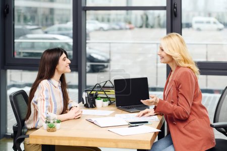 Photo for Two focused women converse at a modern office table. - Royalty Free Image