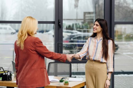Two women shaking hands in an office, sealing a deal.