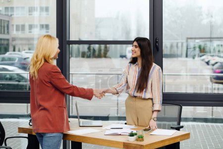 Two hard-working women in an office, sealing a deal through a handshake.