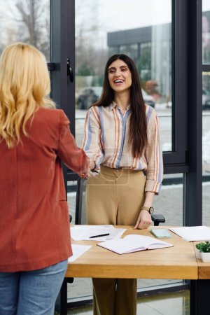 Photo for Two women sealing a deal with a handshake in an office setting. - Royalty Free Image