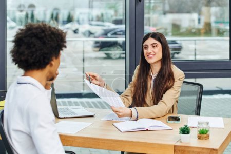 Man and woman engage in conversation at office desk during job interview.
