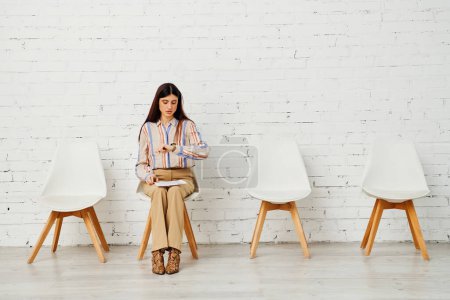 Foto de Una mujer sentada con gracia en una silla frente a una pared de ladrillo texturizado. - Imagen libre de derechos