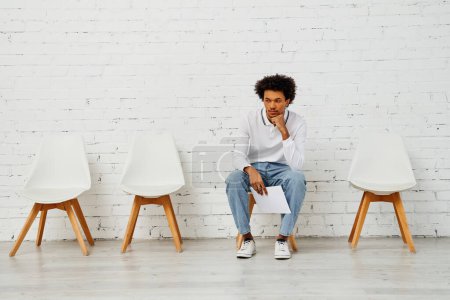 Téléchargez les photos : Homme assis devant une chaise blanche contre un mur de briques. - en image libre de droit
