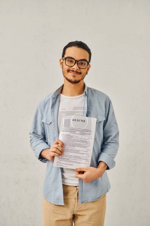 A man standing in front of a white wall, holding resume.