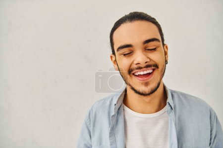 A young man laughs while looking at a blank white backdrop.