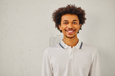Photo for A young man with curly hair smiling in front of a white wall. - Royalty Free Image