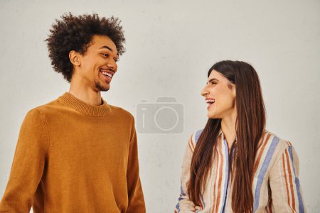 Man and woman laugh happily in front of plain backdrop.