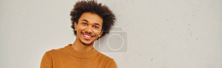 Téléchargez les photos : Jeune homme aux cheveux bouclés sourit devant un mur blanc. - en image libre de droit