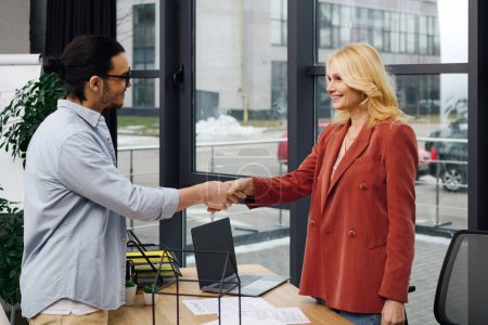 Un hombre y una mujer en una oficina estrechando las manos durante una entrevista de trabajo.