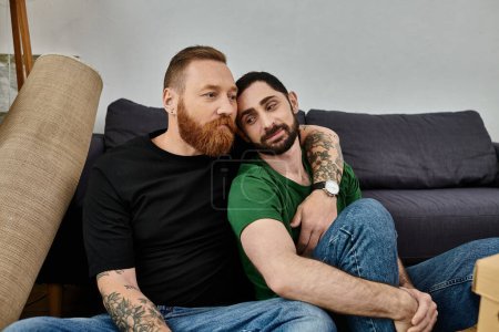A couple of men sit comfortably on top of a couch in their new home