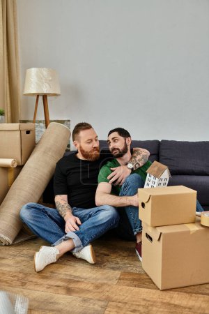 A gay couple relaxes on top of a couch in their new home filled with moving boxes, beginning a new chapter in their lives.