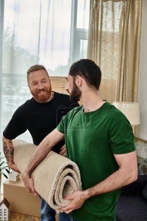 Foto de A happy gay couple stands together in their new living room, surrounded by moving boxes, starting a new chapter in their life. - Imagen libre de derechos
