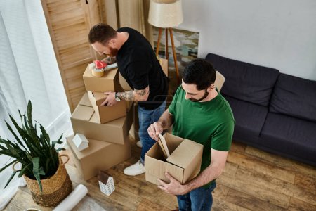 Zwei Männer packen in ihrem neuen Wohnzimmer Kartons aus, voller Liebe und Begeisterung für den gemeinsamen Neuanfang.