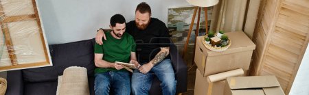 Photo for Two men, part of a loving gay couple, rest atop a sofa amidst moving boxes in new home. - Royalty Free Image