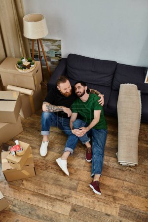Ein Mann und eine Frau, ein verliebtes schwules Paar, sitzen auf dem Boden inmitten von Umzugskartons in ihrem neuen Wohnzimmer.