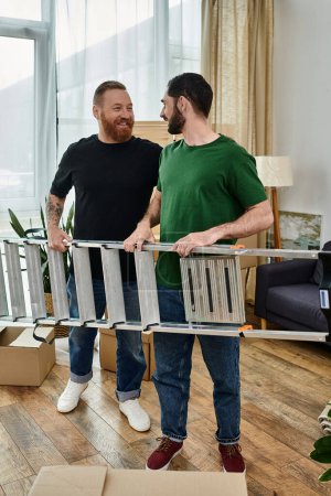 Two men, a gay couple, stand together in their living room and holding ladder, beginning a new chapter in their lives.