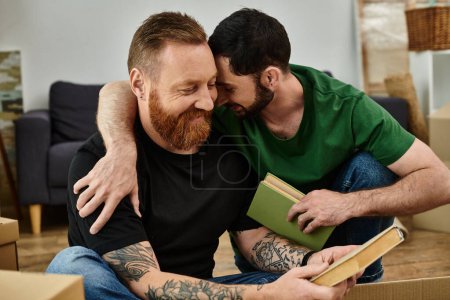 Téléchargez les photos : Two men, a gay couple in love, sitting side by side in their new home surrounded by books, starting a fresh chapter. - en image libre de droit