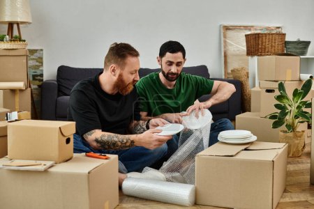 Couple gay amoureux, assis au-dessus de boîtes, emménageant dans une nouvelle maison, entouré de biens, début d'un nouveau chapitre.