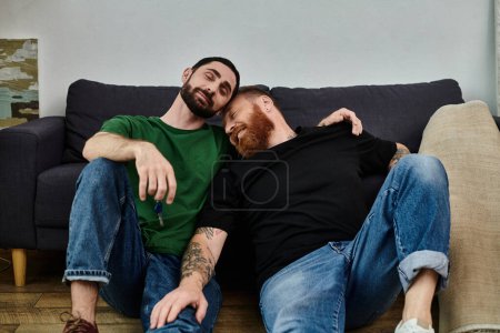Téléchargez les photos : Un couple gay amoureux est assis sur un canapé dans leur nouvelle maison - en image libre de droit
