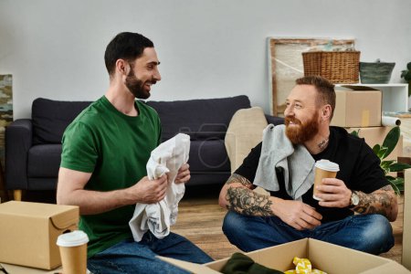 Un couple gay amoureux prend une pause, assis sur un canapé entouré de boîtes mobiles dans leur nouvelle maison.