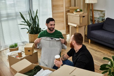 Two men, a gay couple in love, sitting on the floor of their new living room surrounded by moving boxes.