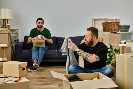 Foto de A gay couple in love relaxes on the couch in their new home, surrounded by moving boxes, embracing their fresh start. - Imagen libre de derechos