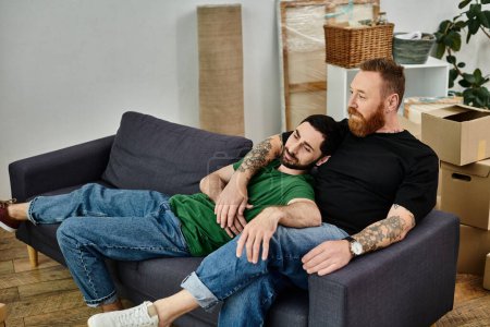 Téléchargez les photos : Un couple gay se détendre sur un canapé au milieu de leurs tâches de déménagement, exsudant le confort partagé et la compagnie. - en image libre de droit