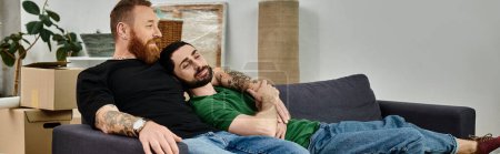 Foto de Dos hombres, una pareja gay, se sientan cerca en un sofá en medio de cajas móviles, simbolizando el amor, nuevos comienzos y unión.. - Imagen libre de derechos