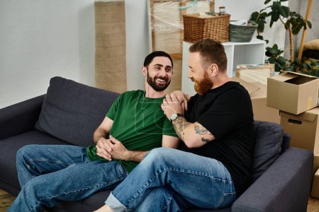 Ein schwules Paar hockt auf einer Couch und teilt einen liebevollen Moment inmitten ihrer Umzugskartons in ihrem neuen Zuhause.