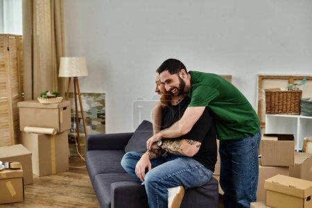 A man and a woman, a gay couple, are seated on a couch in a living room surrounded by moving boxes, starting a new life together.