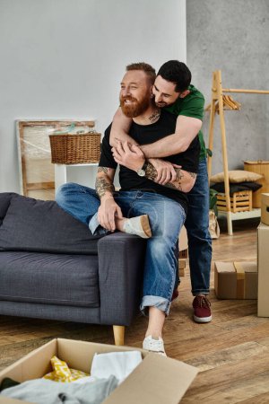 Un par de hombres se sientan encima de un sofá de felpa, abrazando su amor en medio de un movimiento caótico en su nuevo hogar.