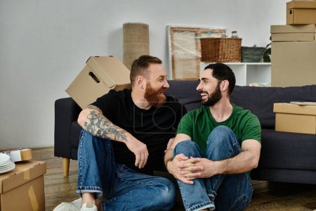 Foto de Una pareja gay, enamorada, se sienta encima de un sofá rodeada de cajas móviles, comenzando una nueva vida juntos. - Imagen libre de derechos