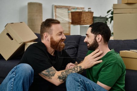 Ein schwules verliebtes Paar sitzt, umgeben von Umzugskartons, auf einer Couch in ihrem neuen Zuhause und beginnt gemeinsam ein neues Kapitel.