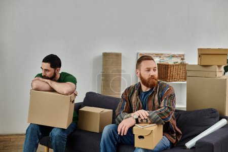 Photo for A gay couple sit atop a couch amidst moving boxes, having disagreement in their new home. - Royalty Free Image