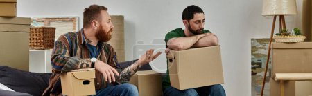 Téléchargez les photos : Hommes gays entourés de boîtes de déménagement dans leur nouvelle maison, ayant un désaccord et un malentendu - en image libre de droit