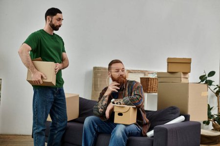 Téléchargez les photos : A man sits on a couch surrounded by boxes, reflecting on his new beginnings in a new home with his partner. - en image libre de droit
