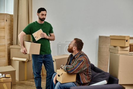 Un homme se tient à côté de son partenaire, tenant des boîtes alors qu'ils se préparent à emménager dans une nouvelle maison remplie d'amour.