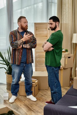 Photo for A gay couple in love stands in their new living room, surrounded by moving boxes, having disagreement and misunderstanding - Royalty Free Image