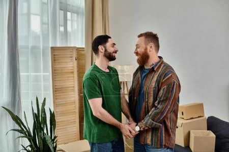 Gay couple in love stands by each other in a living room filled with moving boxes, starting a new chapter in their life together.