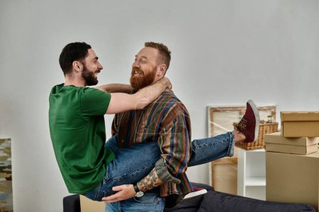 Foto de Una pareja gay enamorada, de pie al lado del otro, empezando una nueva vida en su nuevo hogar rodeada de cajas de reubicación. - Imagen libre de derechos