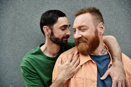 Téléchargez les photos : Gay couple in casual attire embracing in a heartwarming hug against a grey wall. - en image libre de droit